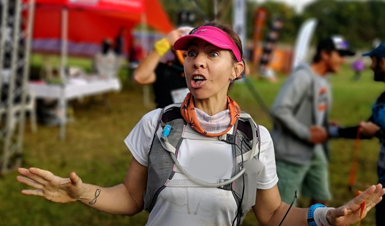 A trail runner at the start, arms spread mid-sentence, the field gathering behind her